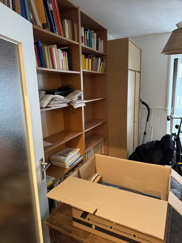 Ein Bücherregal mit Papieren auf den Böden, davor ein geöffneter Umzugskarton, bei einem Umzug in Düsseldorf