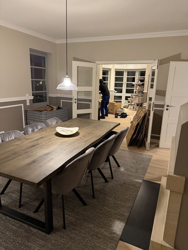 Ein fertig eingeräumtes Esszimmer, der Tisch ist gedeckt, nebenan werden leere Kartons zusammengefaltet
