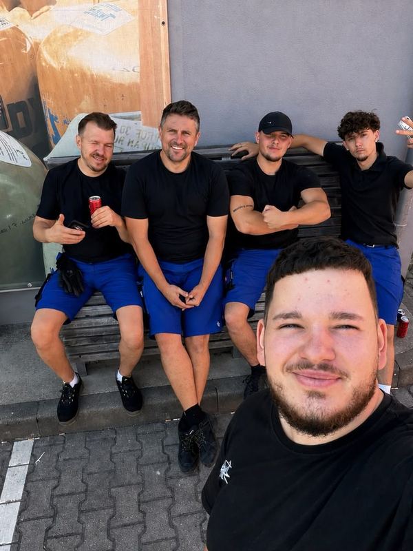 Auf einer sonnigen Bank sitzen fünf Mitarbeiter in Arbeitskleidung zusammen