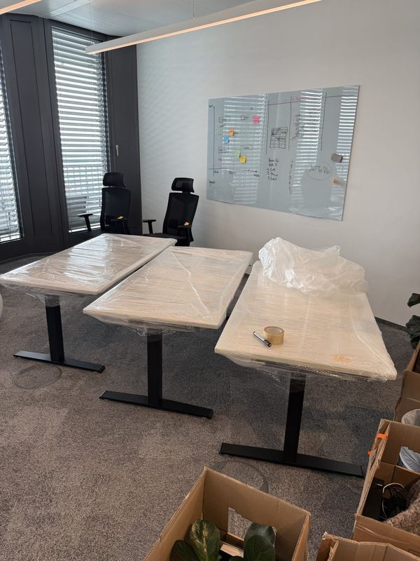 Im Büro stehen drei höhenverstellbare Schreibtische mit folierten Platten nebeneinander