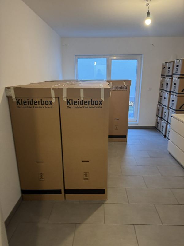 Zwei Kleiderboxen neben einem Kartonstapel in einem leeren Raum