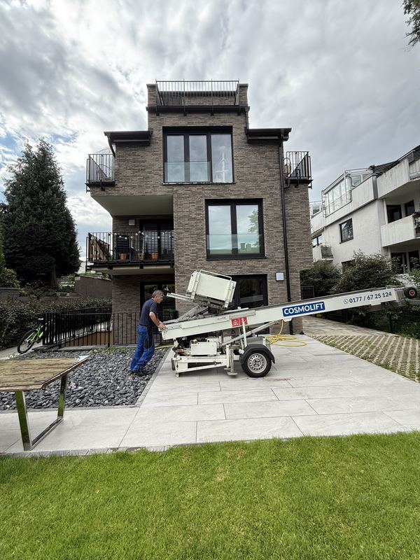 Vor einem Wohnhaus richtet ein Mitarbeiter auf der Einfahrt einen Möbellift aus