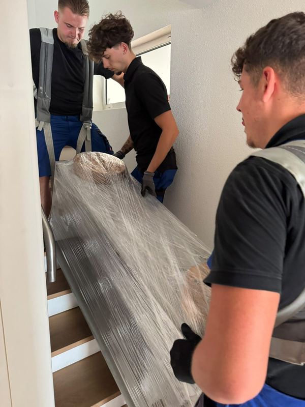 Zu dritt bringt das Team ein in Folie verpacktes Möbelstück die Treppe hinab