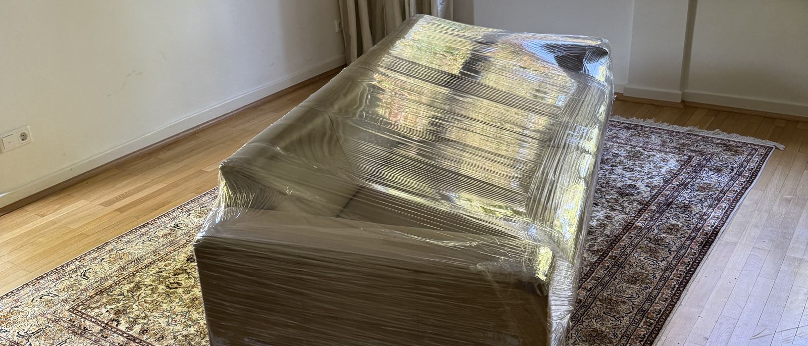 Privatumzug in Düsseldorf: Sofa in Stretchfolie gewickelt auf einem Teppich in einem hellen Wohnzimmer