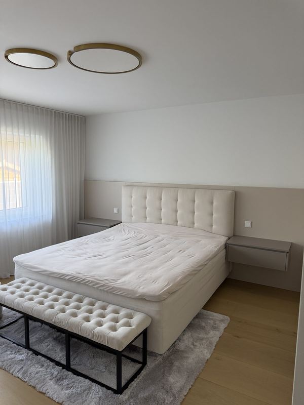 Ein helles Schlafzimmer, darin ein aufgebautes Boxspringbett mit Sitzbank am Fußende