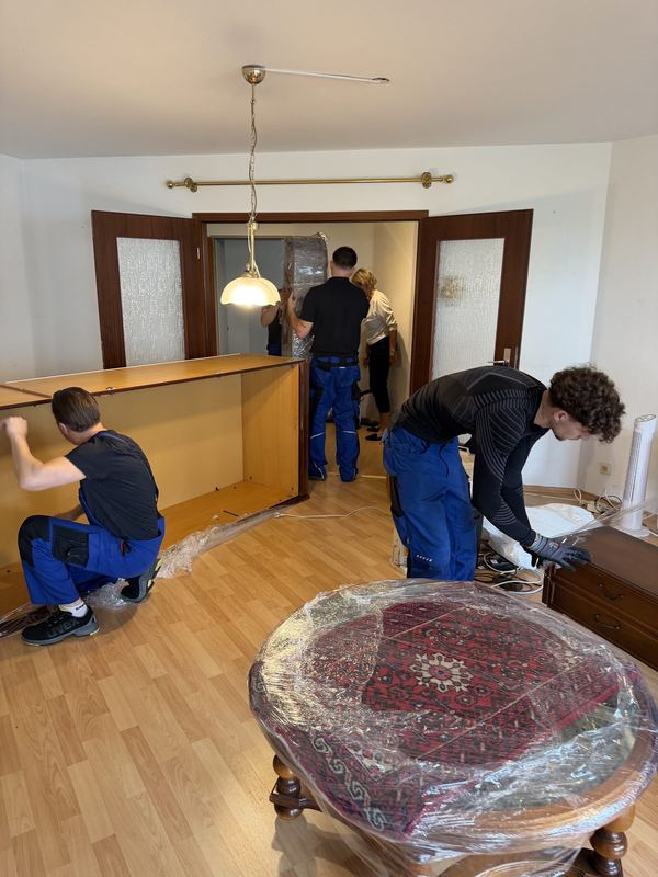 In einem Wohnzimmer setzen vier Kollegen gemeinsam den großen Korpus einer Schrankwand