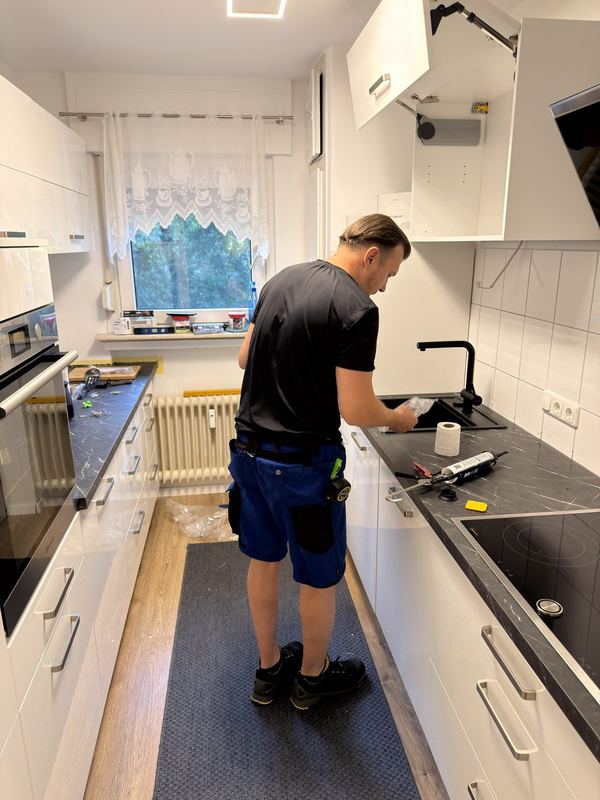 In den Ausschnitt der Arbeitsplatte setzt ein Mitarbeiter eine schwarze Spüle ein