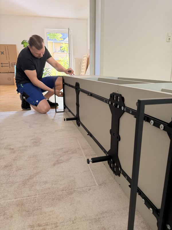 An einem liegenden Sideboard bringt ein kniender Mitarbeiter die Beschläge an