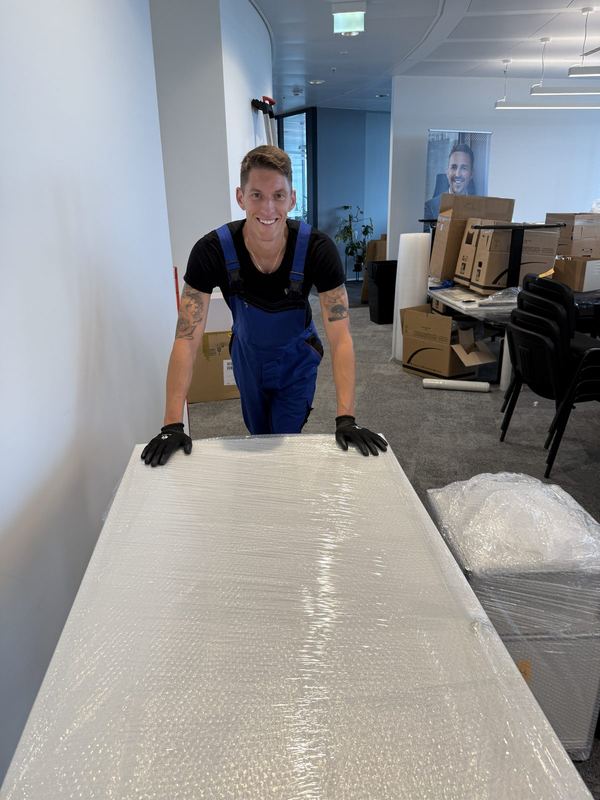 Hinter einer großflächig in Luftpolsterfolie eingepackten Tischplatte steht ein Mitarbeiter