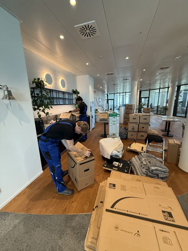 In einem Büro verschließt ein Mitarbeiter einen Umzugskarton, dahinter stehen weitere