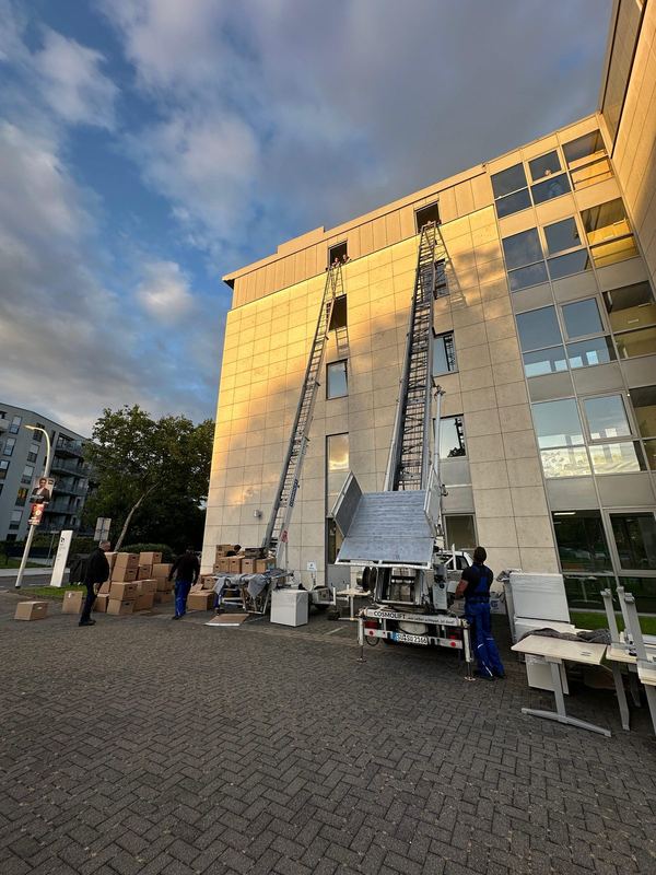 An einem Bürogebäude stehen zwei ausgefahrene Möbellifte Seite an Seite vor der Fassade